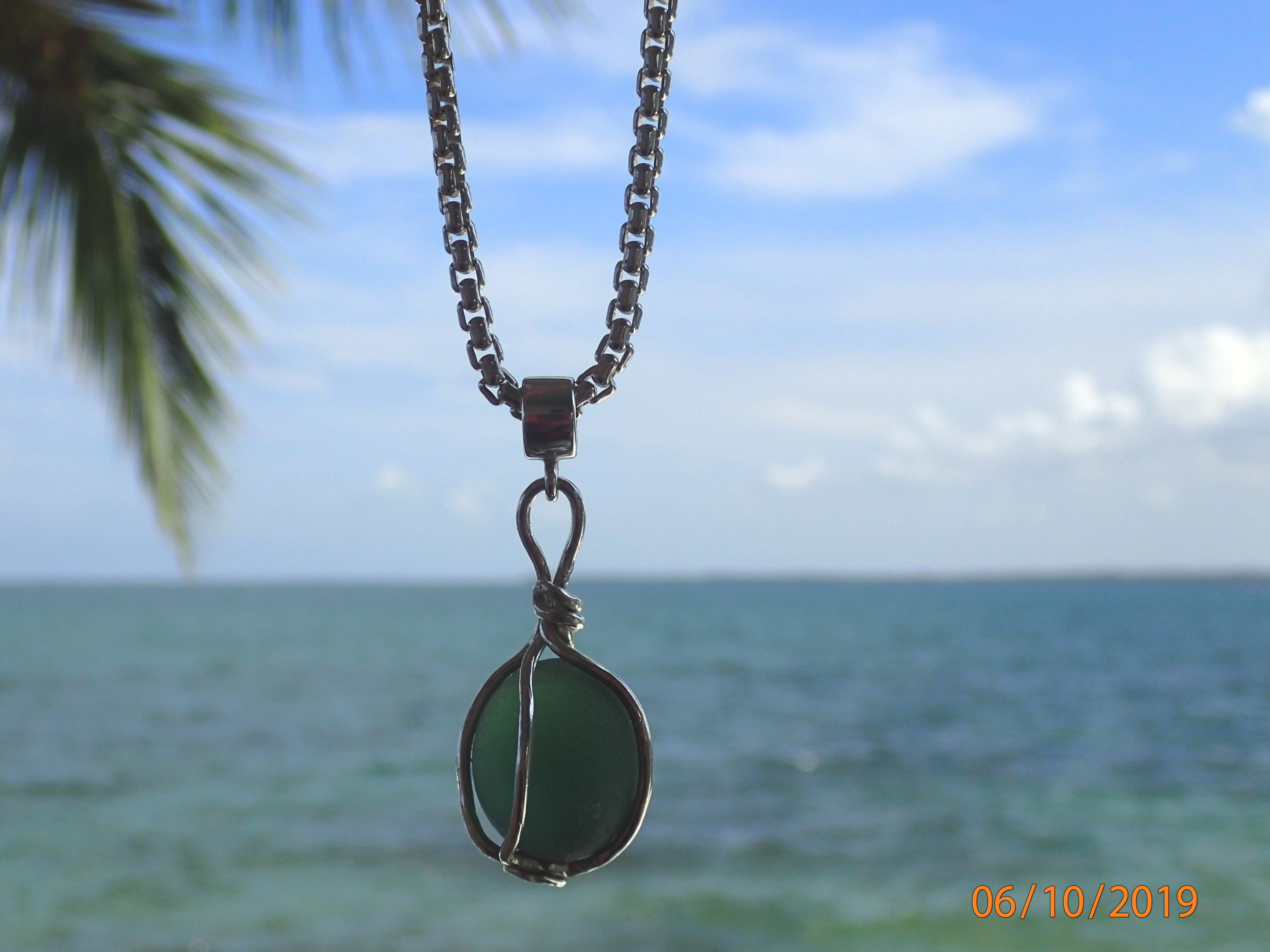 Deep green circular antique seaglass nugget like an antique glass float caged in a sophisticated sterling silver frame.